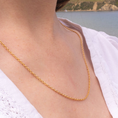 Person wearing a gold necklace with a beach in the background